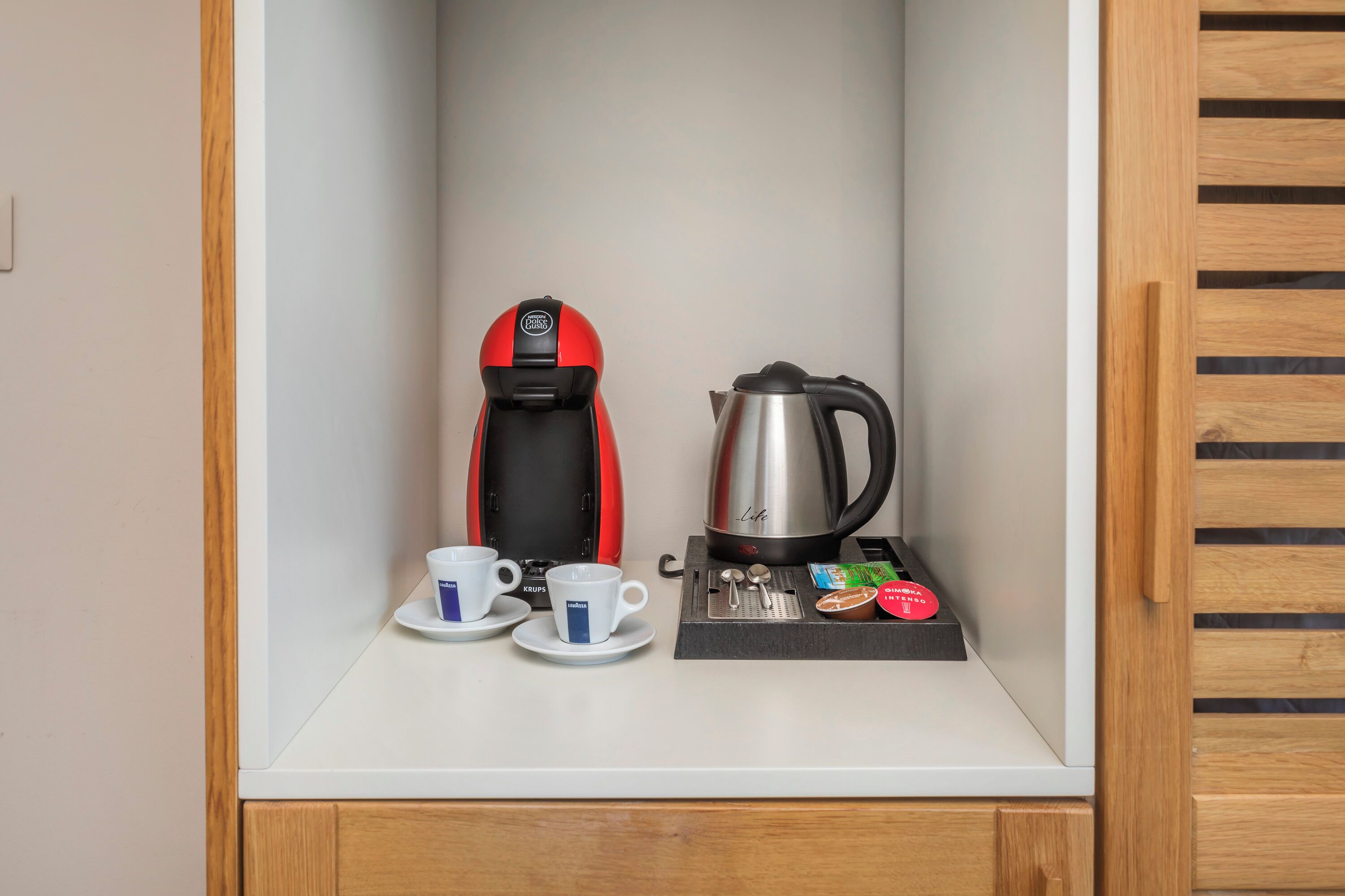Una kitchenette con cafetera, dos tazas, hervidor y una bandeja con condimentos.