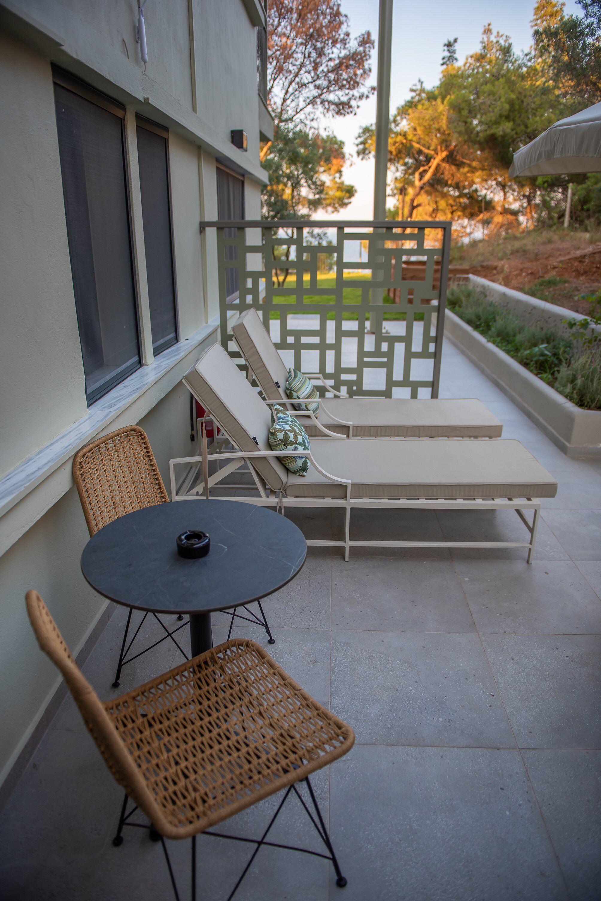 Un patio con una mesa redonda y dos sillas de mimbre, un banco acolchado y una valla decorativa.