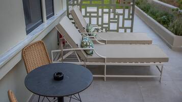 Un patio con una mesa redonda y dos sillas de mimbre, un banco acolchado y una valla decorativa.