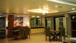 A dining area with wooden tables and chairs, a bar with shelves of bottles, and a large mirror above the counter. - Hotel Sangam Vihar (Saharsa)