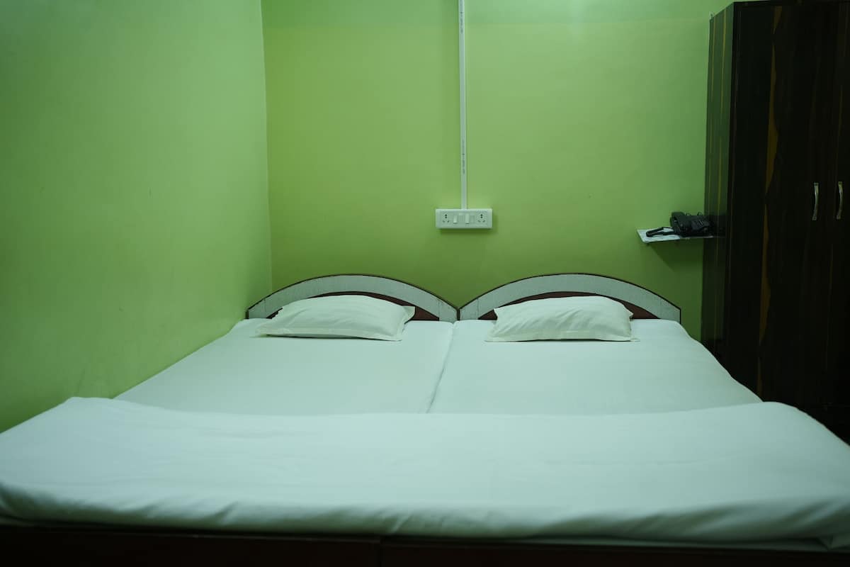A single bed with white bedding in a room with green walls and a wooden wardrobe.
