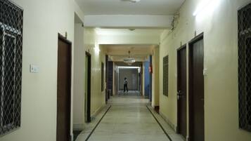 A corridor with doors on both sides, a person walking down the hallway, and a chandelier hanging from the ceiling.