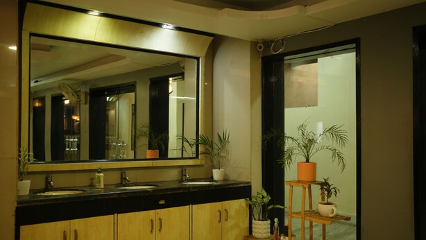 A modern bathroom with a large mirror, wooden cabinets, a black countertop, and multiple potted plants. - Hotel Sangam Vihar (Saharsa)