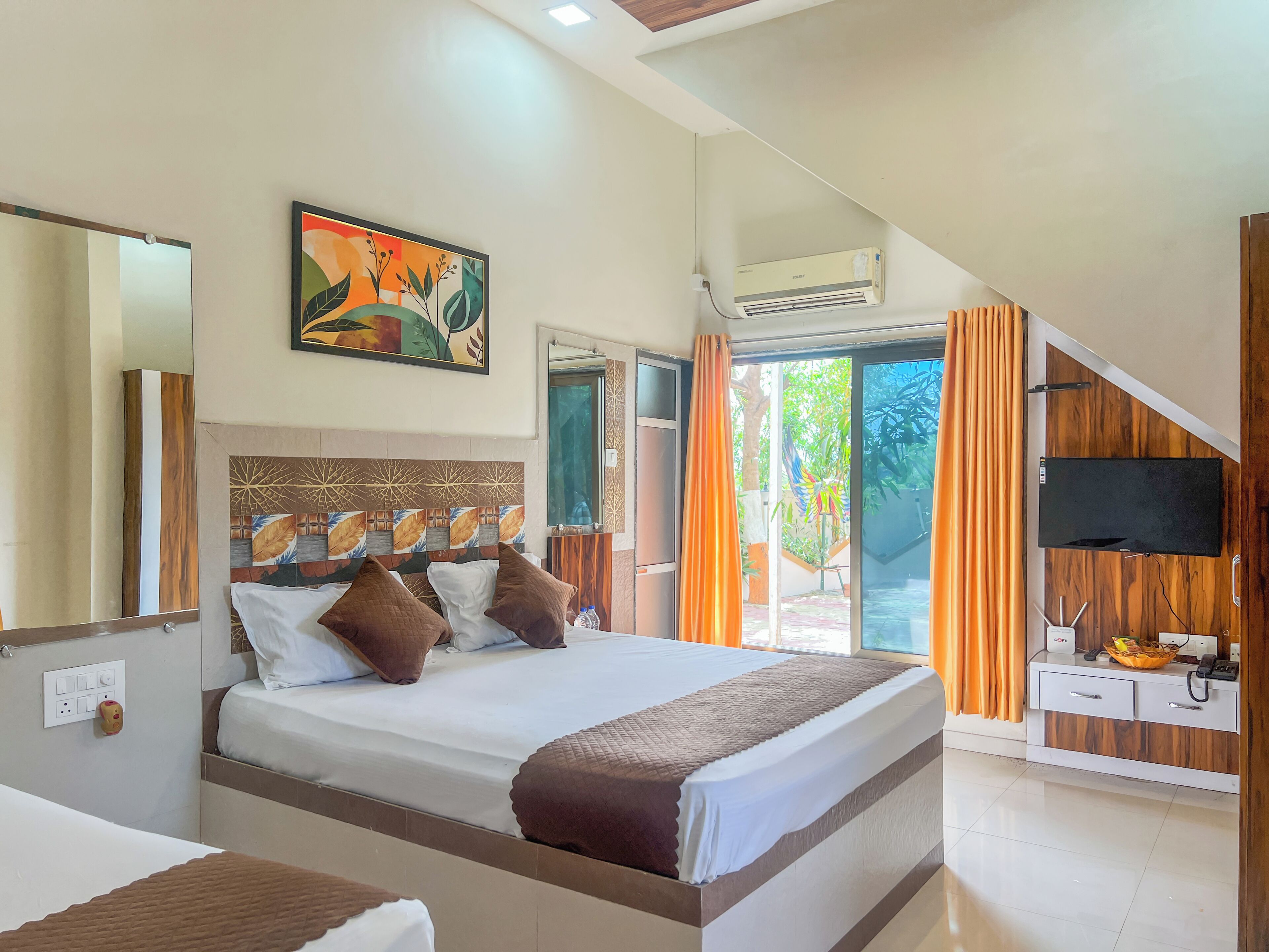 A bedroom with a bed, a painting, an air conditioning unit, a TV, and a desk with a phone.