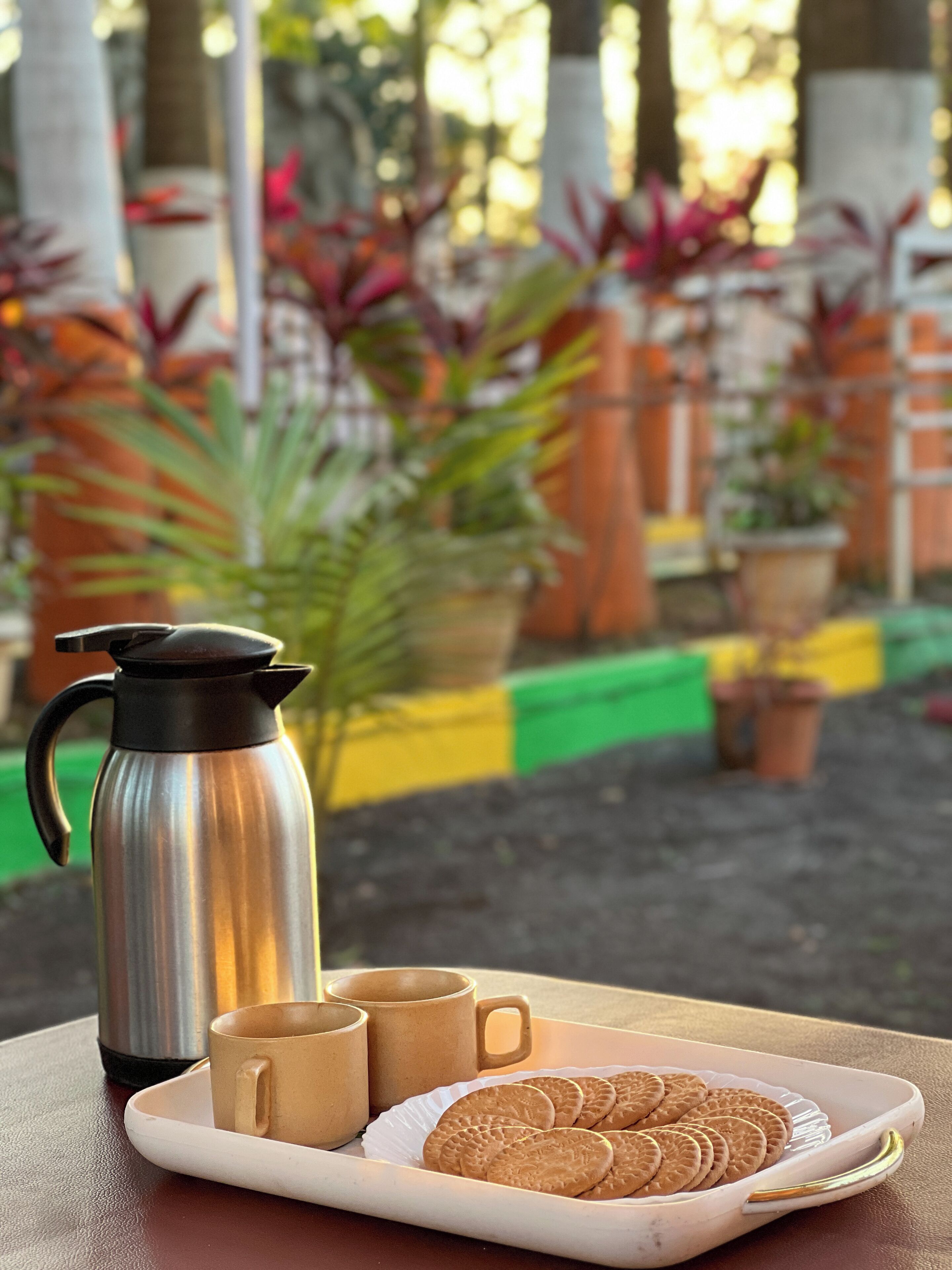 Une table avec une cafetière en acier inoxydable, deux tasses beiges et une assiette de biscuits.