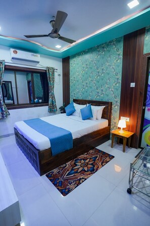 Un dormitorio moderno con cama, ventilador de techo, equipo de aire acondicionado, mesita de noche de madera y alfombra estampada.