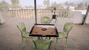 Una mesa con un juego de shuffleboard rodeada de sillas verdes en un balcón con baranda, con vistas a una zona residencial.