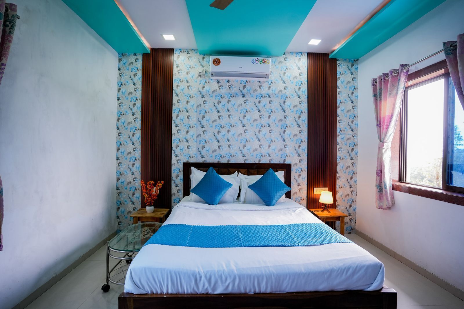 A bedroom with a bed, a nightstand, a window with curtains, and an air conditioning unit on the wall.