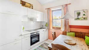 Moderni keittiö, jossa on valkoiset kaapit, sisäänrakennettu uuni sekä ruokailutila, jossa on puinen pöytä ja tuolit.