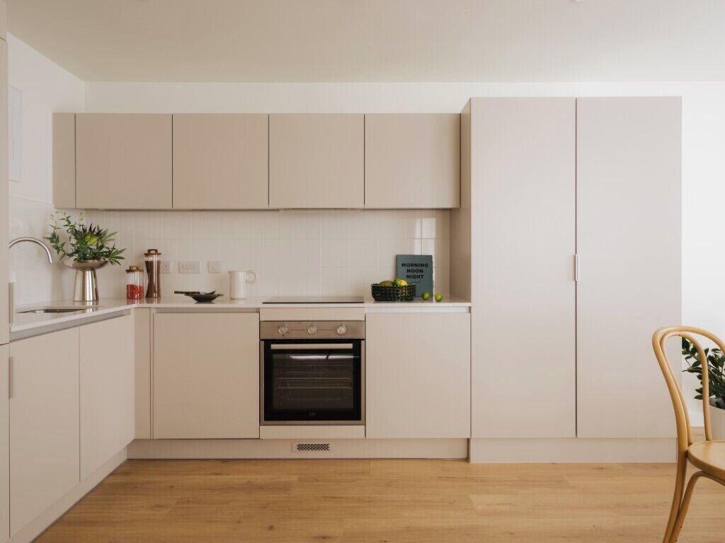 A modern kitchen with white cabinetry, a built-in oven, and a dining area with a wooden table and chair.