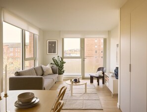 A modern apartment with a sofa, dining table, and chairs, large windows with a city view, and a potted plant. - Leith Linen in Edinburgh (Edinburgh)