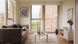 A modern living room with a sofa, a coffee table, and a view of a cityscape through large windows. - Fyfe Marble in Edinburgh (Edinburgh)