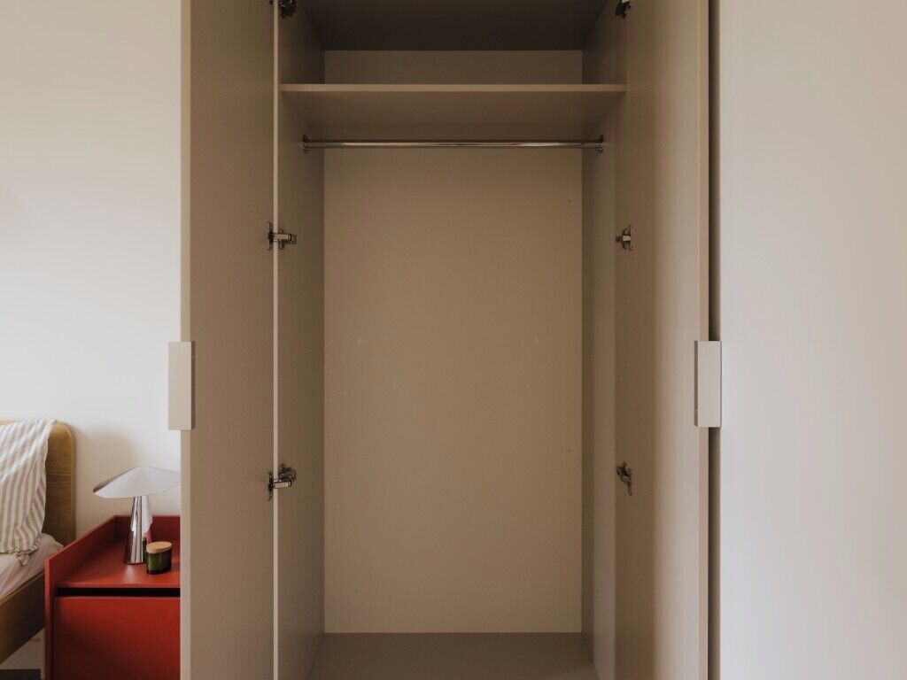 A walk-in closet with a hanging rod and a shelf.