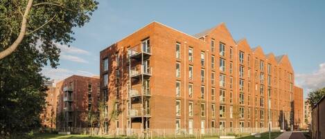 A modern multi-story building with a brick facade, balconies, and a well-maintained lawn area.
