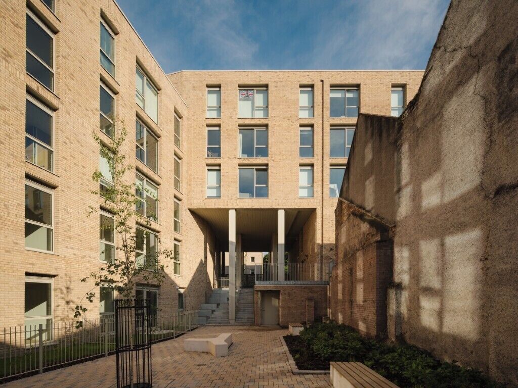 A modern building with a brick facade, large windows, and a central courtyard with steps leading to an entrance.