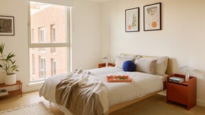 Une chambre avec une grande fenêtre, un lit recouvert d’une courtepointe à rayures, deux œuvres d’art encadrées accrochées au mur et une table de chevet avec une lampe.