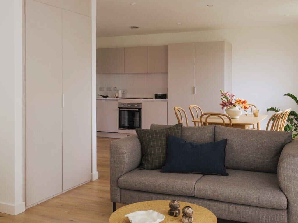 A modern living room with a sofa, a coffee table, and a dining area in the background.