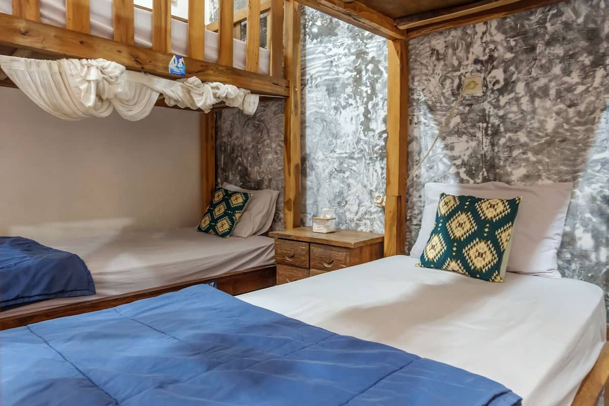 Una habitación con dos camas, techo de madera, pared de piedra y una ventana.