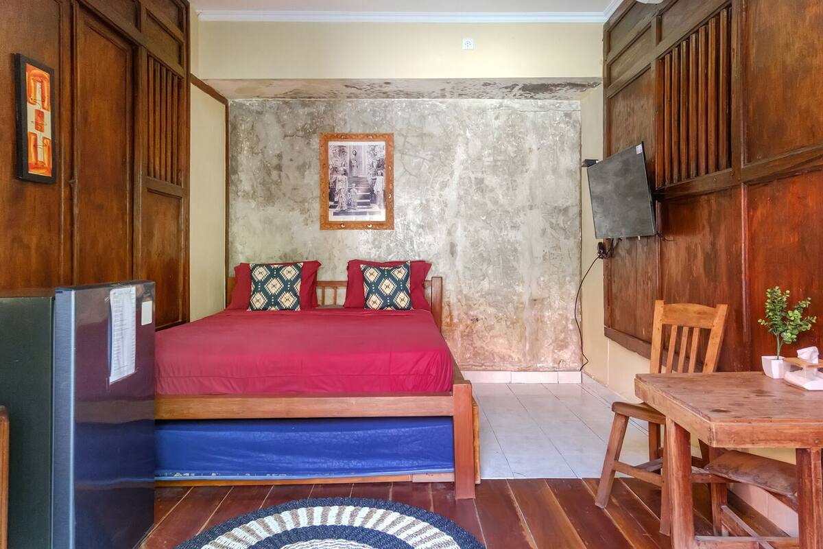 Un dormitorio con cama, un escritorio de madera, una silla, televisor y un cuadro en la pared.