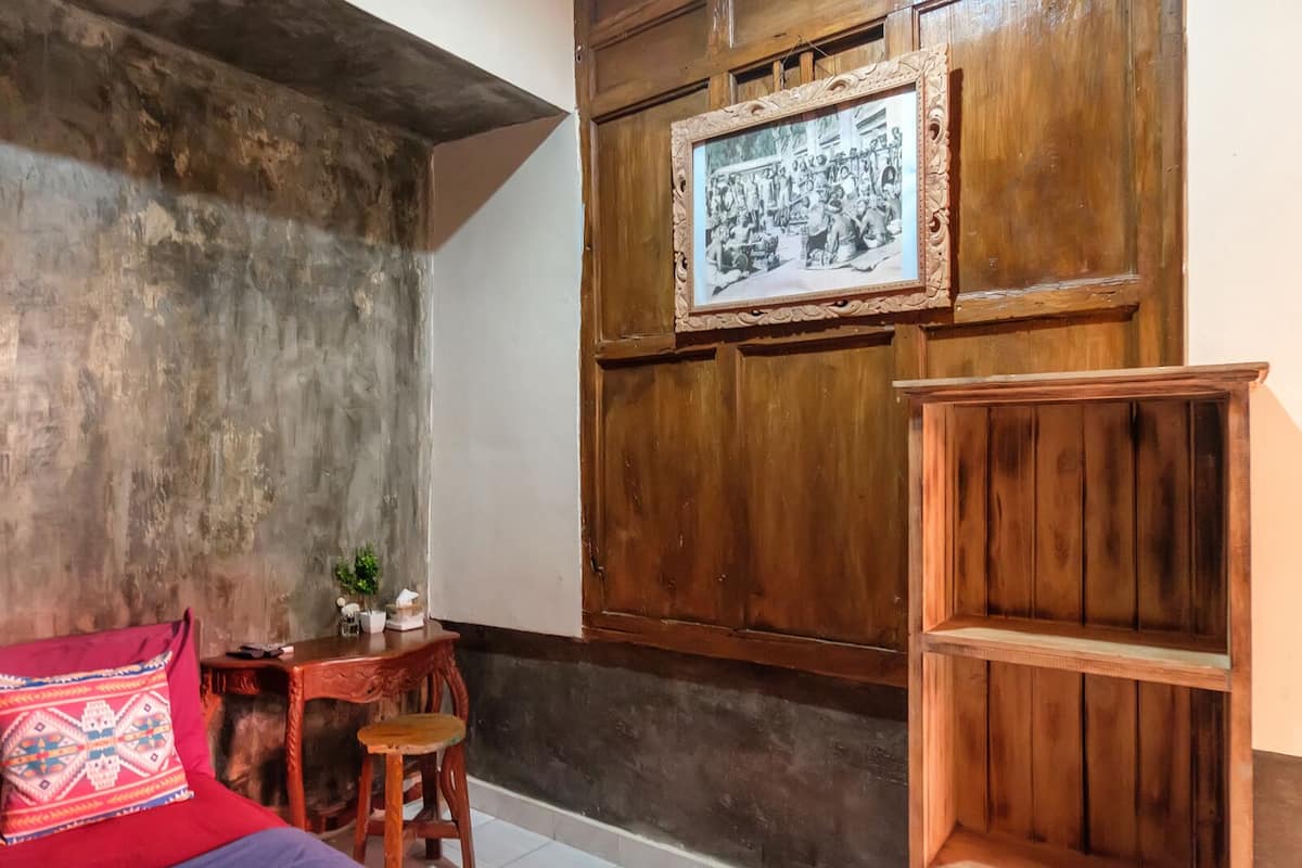 Una habitación con pared de hormigón, un armario de madera, un cuadro enmarco y una mesita con una silla.