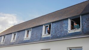 Un bâtiment doté de nombreuses fenêtres, dont certaines sont ouvertes, et on peut apercevoir une personne à travers l’une d’elles.