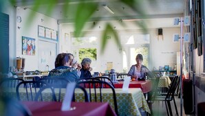 Un espace repas avec des tables et des chaises, une horloge au mur et une fenêtre donnant sur un paysage verdoyant.