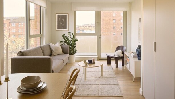 Een modern appartement met een bank, eettafel en stoelen, grote ramen met uitzicht op de stad en een potplant.