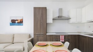 Une cuisine moderne avec des armoires blanches, une hotte en acier inoxydable et un coin repas avec une table dressée pour quatre personnes.