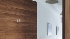 Une porte en bois portant le numéro 38, un couloir aux murs blancs et un luminaire suspendu.