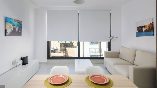 Un salon moderne avec un canapé, une table à manger avec deux assiettes et une grande fenêtre avec des stores.