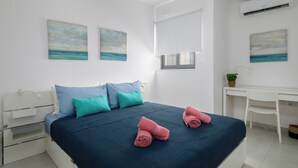 Une chambre à coucher moderne avec un lit, des oreillers, un bureau et des œuvres d’art accrochées aux murs.