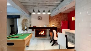 Une table de billard, une cheminée et un mur rouge dans une pièce aux murs en pierre et blancs.