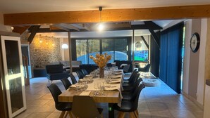 Un espace repas avec une longue table dressée pour six personnes, entourée de chaises noires aux pieds en bois.