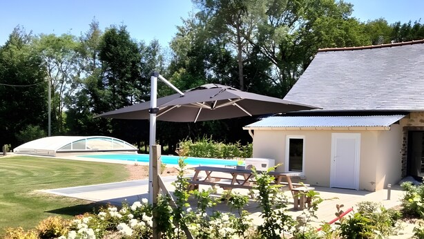 Un jardin avec une piscine, des meubles de patio et un espace abrité avec un parasol.