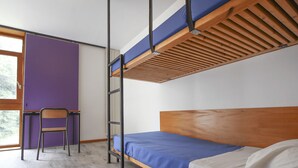 Een stapelbed met een houten hoofdbord en een bureau, met een paars gestucte muur erachter.