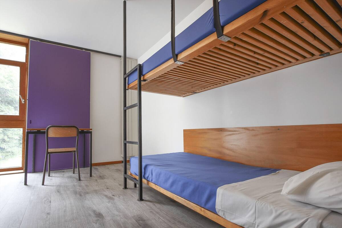 Een stapelbed met een houten hoofdbord en een bureau, met een paars gestucte muur erachter.