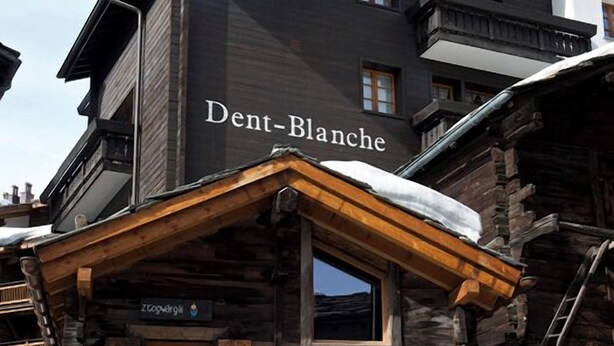 Een houten gebouw met een bord waarop 'Dent-Blanche' staat.