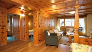 Een houten cabin-interieur met een gezellig woongedeelte, inclusief een bank, fauteuils en een eettafel.