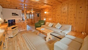 Een gezellig houten blokhut interieur met een bank, een groene fauteuil, een houten tafel en een televisie op een houten dressoir.