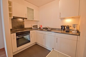 A compact kitchen with white cabinets, a built-in oven, a microwave, a kettle, and a coffee maker. - Haus Viktoria A, Apartment Stockhorn (Zermatt)
