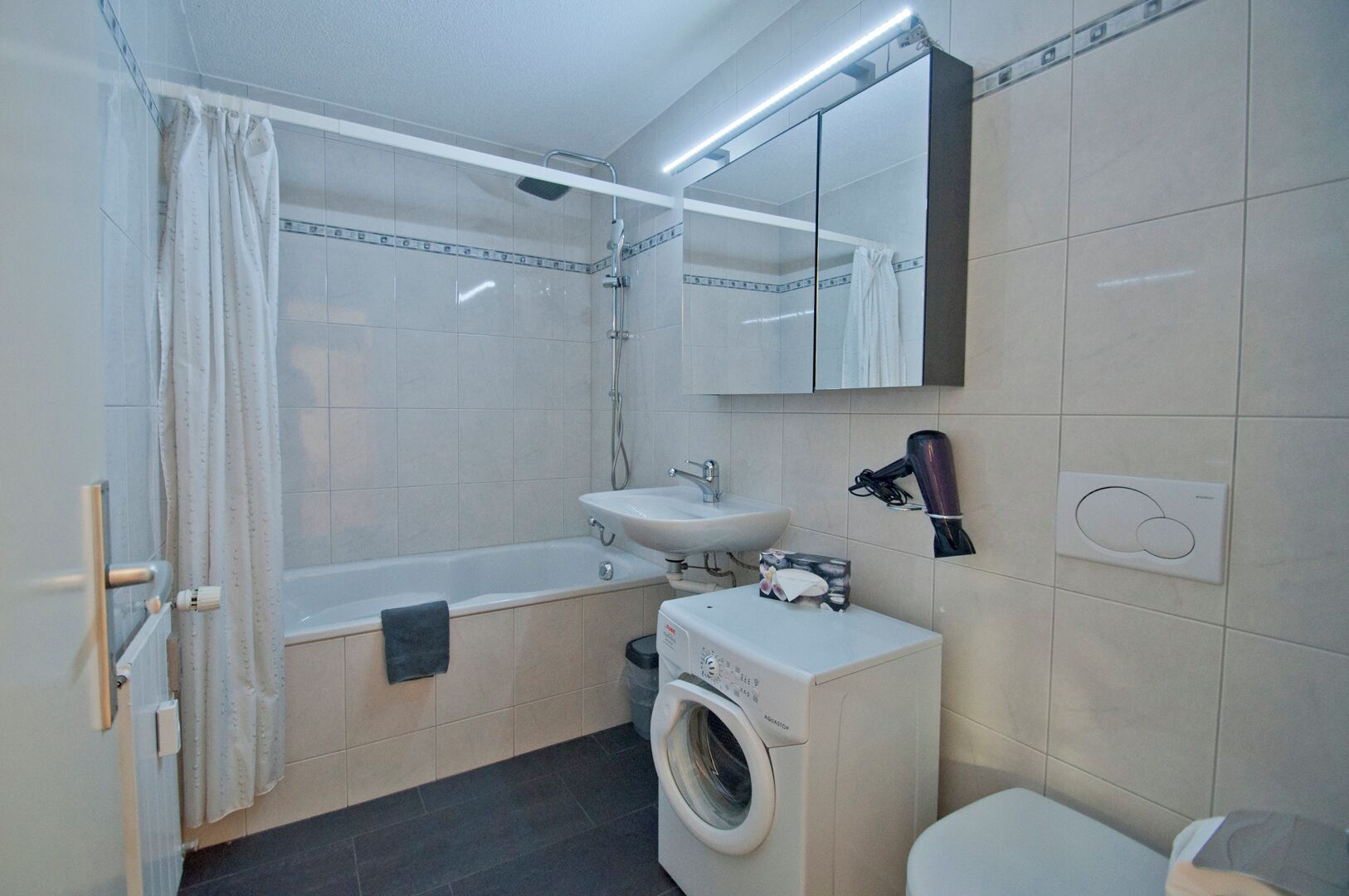 Une salle de bain moderne équipée d’une baignoire, d’un lavabo, d’un miroir, d’un sèche-cheveux et d’un lave-linge.