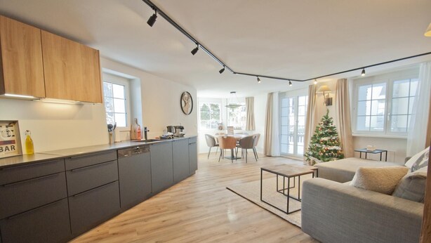 A modern kitchen with a central island, a dining area with a table and chairs, and a living room with a sofa. - Chalet Aeschhorn, Apartment Lucy (Zermatt)