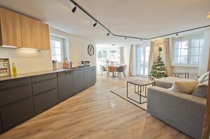 A modern kitchen with a central island, a dining area with a table and chairs, and a living room with a sofa. - Chalet Aeschhorn, Apartment Lucy (Zermatt)