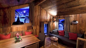 A wooden interior with a dining table, sofa, and a large window with a view of a snowy landscape. - Luxury Chalet Z'Gogwärgji (Zermatt)
