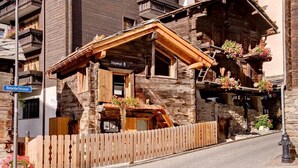 A wooden mountain lodge with a stone facade, wooden balconies with flower boxes, and a wooden fence. - Luxury Chalet Z'Gogwärgji (Zermatt)