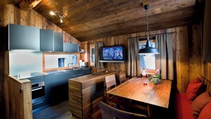 A modern kitchen with a wooden ceiling, a dining area with a wooden table, and a television mounted on the wall. - Luxury Chalet Z'Gogwärgji (Zermatt)