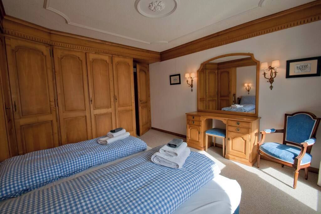 A room with two beds, wooden wardrobe, a desk, a chair, and a mirror.