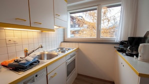 Eine kompakte Küche mit weißen Schränken, einer doppelten Spüle, einer Kaffeemaschine und einem Fenster mit Blick auf Gebäude und Bäume.