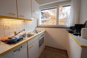 Une cuisine de taille réduite avec des meubles blancs, un évier à deux bacs, une cuisinière et une machine à café.