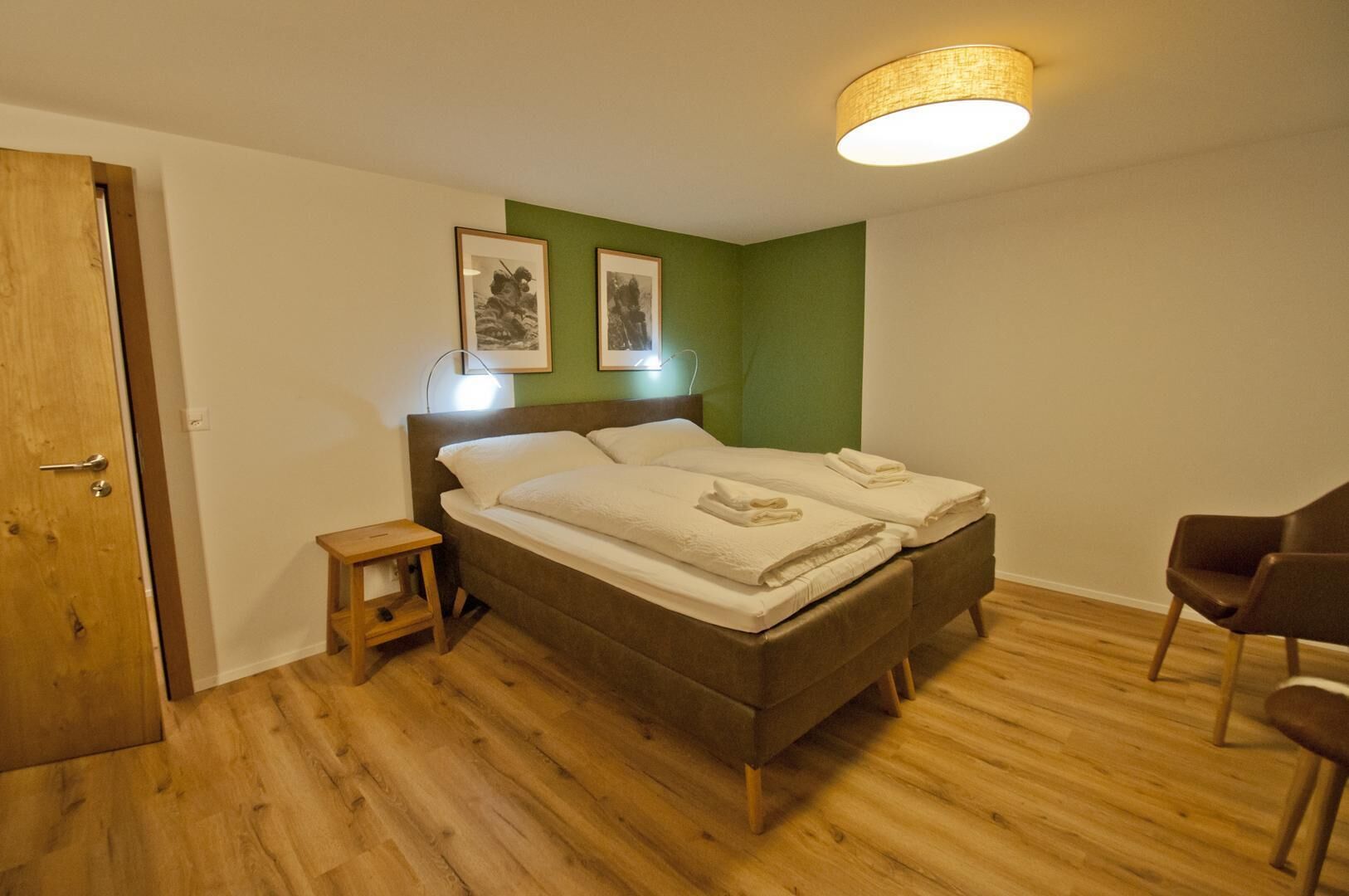 Ein Schlafzimmer mit einem Doppelbett, einem kleinen Nachttisch, einem Sessel und zwei gerahmten Bildern an der Wand.